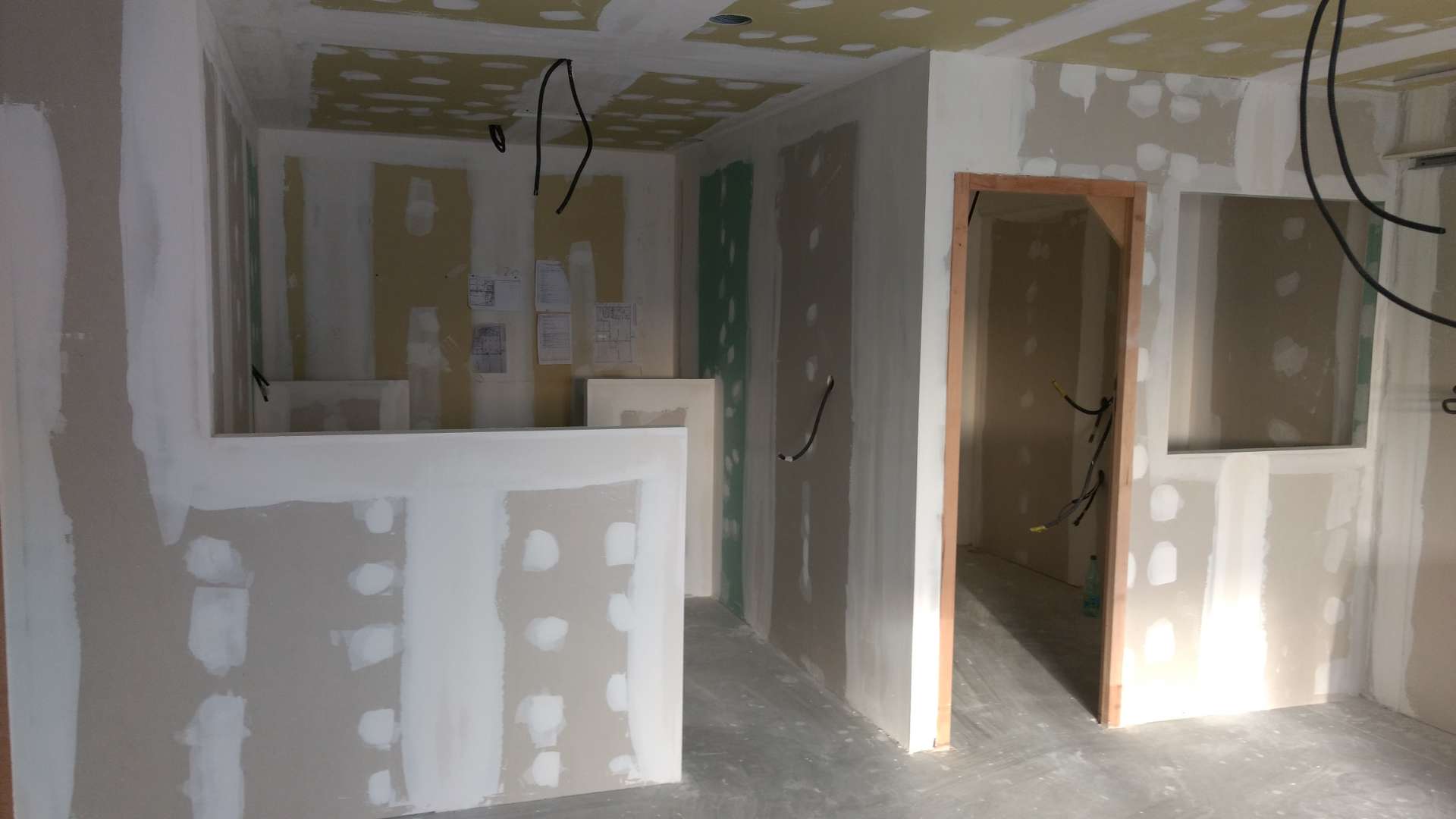 Pièce en travaux avec cloisons de plaques de plâtre, joints blancs, câbles électriques pendant du plafond et porte sans vantail.